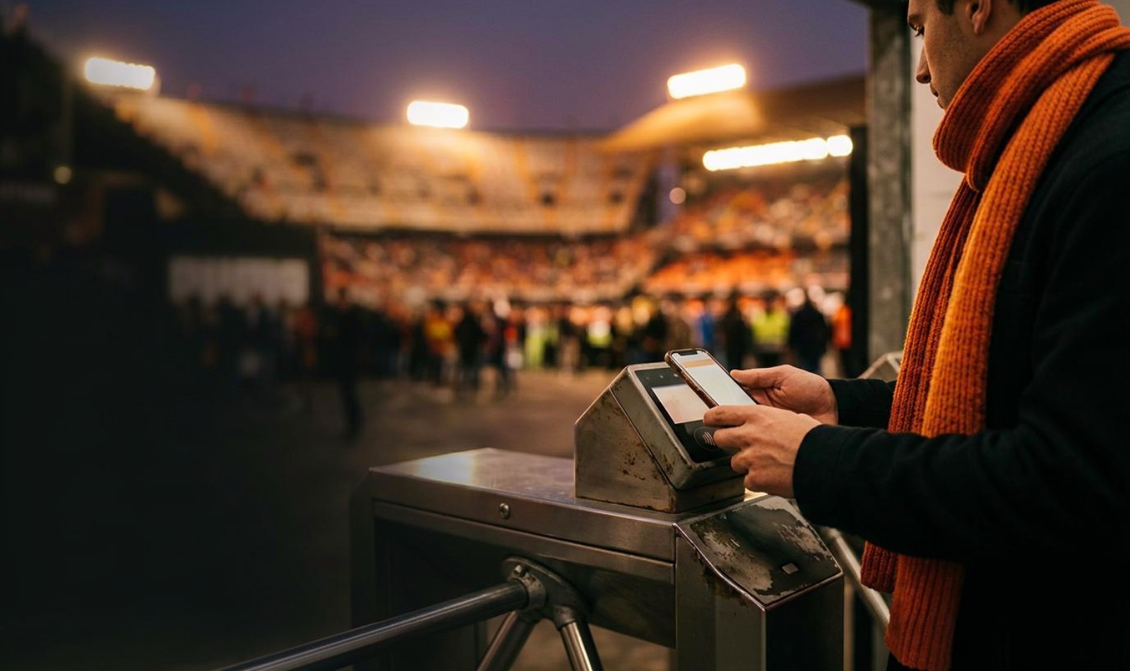 Sports fan in an orange scarf scanning a digital membership pass on their phone at a stadium gate